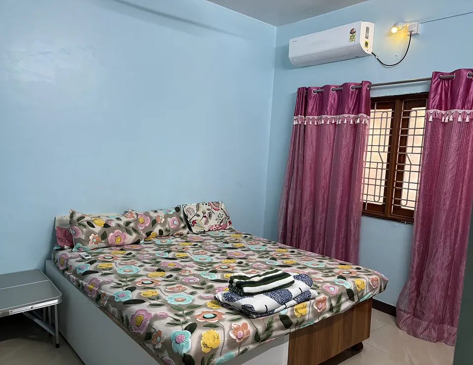 Bedroom with a king-size bed, floral bedsheet, split AC, ceiling fan and folded towels