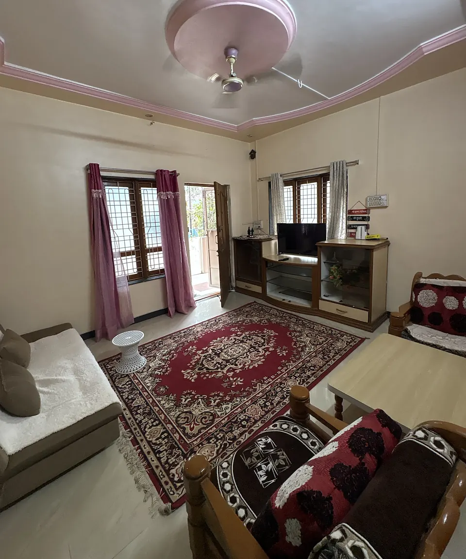 The hall at Chaitanya Peaceful Stay, with a red carpet, a sofa-cum-bed, wooden sofa chairs and a TV unit